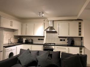 uma cozinha com armários brancos e um sofá na sala de estar em Modern 1 bedroom apartment close to Penzance town centre. em Penzance