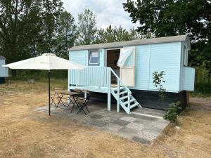 Tiny Beach House في Barkelsby: منزل صغير زرقاء مع طاولة ومظلة