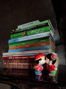 a stack of books with two dolls sitting on a shelf at Вила Перуле Villa Perule - Handmade cozy wooden villa in the Rhodope mountain in Shumnatitsa