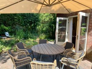 una mesa de madera y sillas con sombrilla en el patio en Huisje aan de Bosrand - Veluwe, en Epe