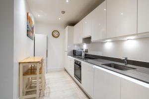 a kitchen with white cabinets and a wooden stool at Stylish 2 bedroom Apartment in Central london in London