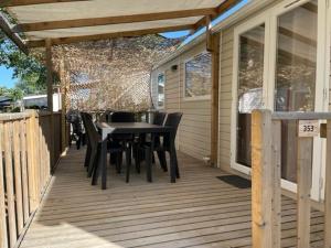une terrasse en bois avec une table et des chaises. dans l'établissement Mobil-home (Clim, Tv)- Camping Narbonne-Plage 4* - 022, à Narbonne-Plage
