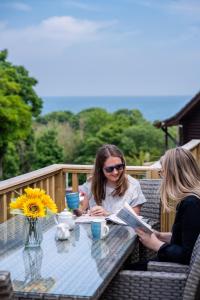 twee vrouwen zitten aan een tafel een boek te lezen bij Watermouth Lodges in Ilfracombe