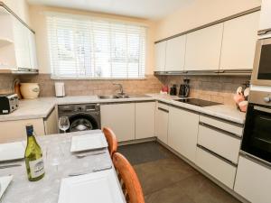 una cocina con armarios blancos y una mesa con una botella de vino en Leisure Cottage en Kirkby Stephen