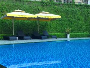 a pool with chairs and umbrellas next to a hedge at Bcons Riverside Hotel Binh Duong in Thu Dau Mot