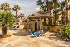 a patio with chairs and an umbrella and palm trees at Villagg tal-Fanal in Għasri