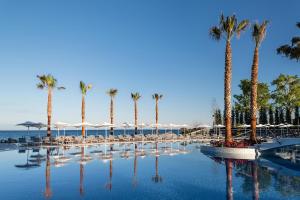 una piscina con palmeras, sillas y sombrillas en Potidea Palace Hotel, en Nea Potidaea