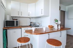 une cuisine avec des placards blancs et un comptoir avec deux tabourets dans l'établissement Bord de plage - Studio en front de mer, au Lavandou 2 autres photos