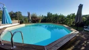 a large swimming pool with a wooden deck and umbrella at La Libellule, piscine, climatisation, wifi, vue ,jardin ,parking in Le Vigan