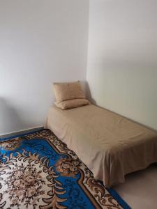 a bed with a pillow on top of a rug at Un appartement à proximité de la corniche Hoceima pour les familles in Al Hoceïma