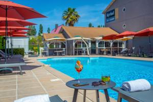 a pool with tables and umbrellas in front of a hotel at KYRIAD MARSEILLE EST - Aubagne Gémenos in Gémenos