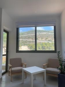 a living room with two chairs and a table and a window at במורד ההר in Shelomi