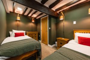 two beds in a bedroom with green walls and red pillows at Spacious, luxury town centre Granary conversion in Stamford
