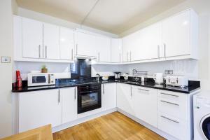 - une cuisine blanche avec des armoires blanches et des appareils noirs dans l'établissement Bloomsbury Pad, à Londres