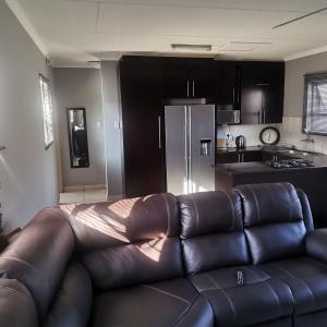 a living room with a leather couch in front of a kitchen at Pablo and Sons Apartments in Polokwane