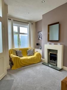a living room with a yellow couch in front of a fireplace at Tithebarn Townhouse in Poulton le Fylde