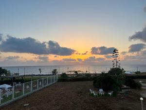 a sunset over the ocean with two chairs and a fence at דירת גן על הים בנהריה in Nahariyya