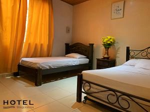 a hotel room with two beds and a vase of flowers at El Hotel Tisquesusa in Girardot