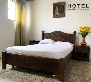 a bedroom with a wooden bed with white sheets at El Hotel Tisquesusa in Girardot