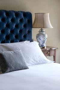 een bed met een blauw hoofdeinde en een tafel met een lamp bij Tenuta Bussia - Wine Relais & Spa in Monforte dʼAlba