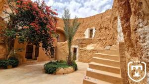 a stone building with stairs and a tree and flowers at Touring Club MARHALA MATMATA in Matmata