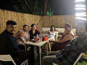 een groep mensen die rond een tafel in een achtertuin zitten bij Hostell One - A complete backpacker & Coworking Hub in Pune