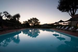 a swimming pool with chairs and a sunset in the background at Agriturismo I Pini in San Gimignano