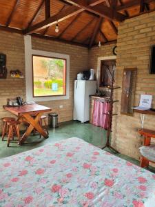 a room with a bed and a table and a refrigerator at Chalés Bela Vista in São Thomé das Letras