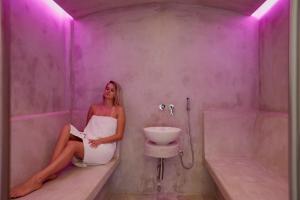 a woman sitting in a bathroom with a sink at Kouros Village Hotel - Adults Only in Perissa