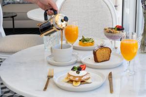 a table with pancakes and orange juice and a person using a tea kettle at Lilases Boutique House & Garden in Mora