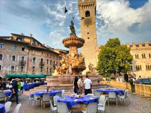 una fuente con mesas y sillas azules y una torre del reloj en Appartamento al Castello en Trento