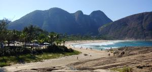 a beach with people on it with mountains in the background at Itacoatiara - Apartamento com café da manhã ao lado da praia in Niterói