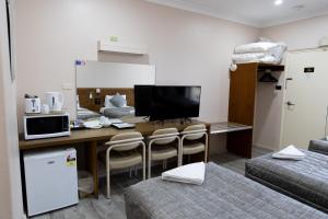 a room with a desk with a television and two beds at Garden Motor Inn Gundagai in Gundagai