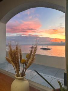 Un jarrón con flores en una ventana con un barco en el agua. en Moana Beach House, en Moalboal