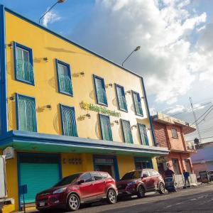dwa samochody zaparkowane przed żółtym budynkiem w obiekcie Hotel Reynieri w mieście Comayagüela