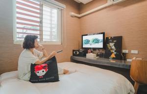 a woman sitting on a bed holding a cell phone at Royal Rose Hotel Taipei Station in Taipei