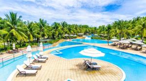 uma piscina de resort com cadeiras e guarda-sóis e palmeiras em Sealinks city - Tvila em Phan Thiet