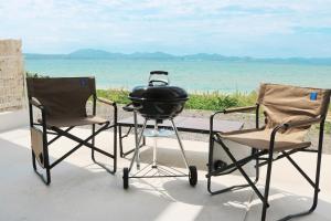 a grill and two chairs on a patio with the ocean at Beach front studio -NagoNago- in Nago