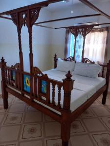 a wooden canopy bed with white sheets and pillows at Rhino Apartment Watamu in Watamu