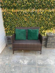 a brown wicker bench with two green pillows at Summer guest house with hottub and BBQ area in Winchmore Hill