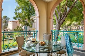 uma varanda com uma mesa de vidro, cadeiras e uma árvore em Al Raha Beach Hotel em Abu Dhabi