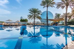 a swimming pool with palm trees and a building at Al Raha Beach Resort & Spa in Abu Dhabi