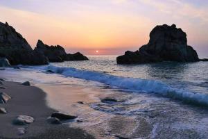 einen Sonnenuntergang am Strand mit Felsen im Wasser in der Unterkunft Trilocale IMMinens mari in Copanello