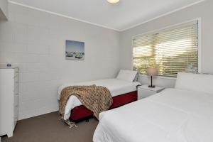 Cette chambre blanche dispose de deux lits et d'une fenêtre. dans l'établissement Hidden Away - Tauranga Bay Holiday Unit, à Mahinepua