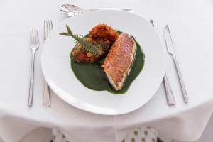 a white plate with a piece of fish on a table at Villa Sainte Anne in Porquerolles