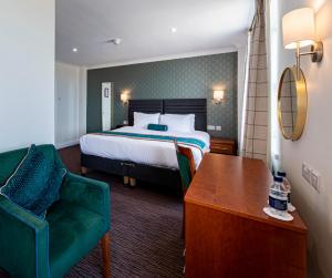 um quarto de hotel com uma cama e uma cadeira verde em The Beaches Hotel em Prestatyn