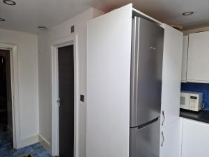 una nevera de acero inoxidable en una cocina con armarios blancos en Studio Flat with kitchen and toilet included, en Dagenham