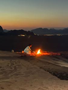 a man sitting next to a fire on the beach at Obeid's Bedouin Life Camp in Wadi Rum