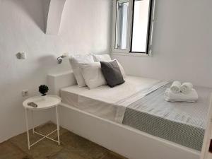 a small white bedroom with a bed and a table at Sunny Stone Tinos House in Tinos