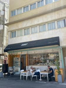 two people sitting at tables in front of a building at Haneemanim Apartments in Haifa